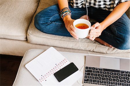 Woman wearing jeans sitting on a sofa in front of a laptop computer, holding a mug. Foto de stock - Sin royalties Premium, Código: 6118-08729161