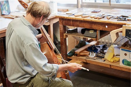 picture of the blue playing a instruments - A violin maker in his workshop playing an instrument with a bow, tuning and finishing. Stock Photo - Premium Royalty-Free, Code: 6118-08729263