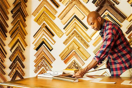 shop interior - Man working at a picture framers, a large selection of frames on the walls. Stock Photo - Premium Royalty-Free, Code: 6118-08729330