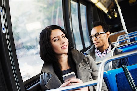 A young man and a young woman sitting on public transport holding their cellphones and looking around. Stock Photo - Premium Royalty-Free, Code: 6118-08842147