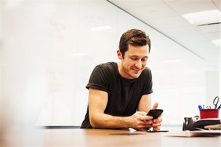 simsearch:6118-08243810,k - A young man sitting in a classroom at a table and looking down at a cellphone. Stock Photo - Premium Royalty-Free, Code: 6118-08842198