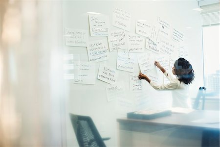 A woman standing in an office arranging pieces of paper pinned on a whiteboard. Photographie de stock - Premium Libres de Droits, Code: 6118-08842120