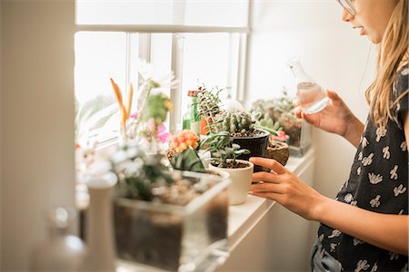 Girl tending plants on a sunny windowsill. Stock Photo - Premium Royalty-Free, Code: 6118-08827461