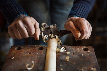 Man standing in a workshop, holding a plane, planing and shaving a piece of wood in a clamp. Stock Photo - Premium Royalty-Free, Code: 6118-08947796