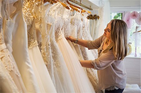simsearch:6118-08202525,k - A sales assistant in a wedding dress shop, looking through the gowns hanging in the rails. Stock Photo - Premium Royalty-Free, Code: 6118-08971420
