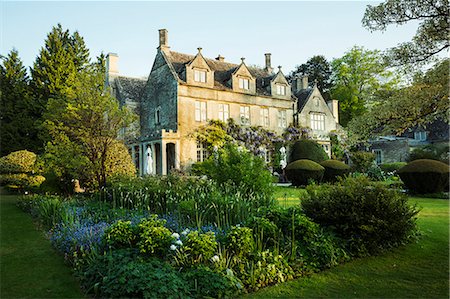 Exterior view of a 17th century Cotswold stone country house from a garden with flower beds, shrubs and trees. Stockbilder - Premium RF Lizenzfrei, Bildnummer: 6118-08971531