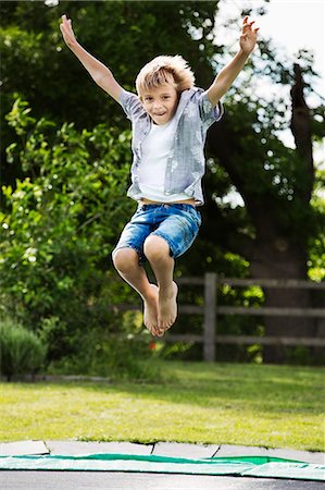 Boy wearing shirt and denim shorts jumping on a trampoline in a garden. Stock Photo - Premium Royalty-Free, Code: 6118-08971638