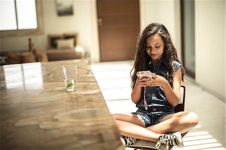 A girl sitting looking at a mobile phone screen. Stock Photo - Premium Royalty-Free, Code: 6118-08991455