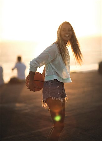 Young woman standing in front of a sunset holding a basketball. Stock Photo - Premium Royalty-Free, Code: 6118-08991632
