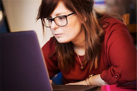 simsearch:6113-07565805,k - A young woman seated using her laptop leaning towards the screen to read content. Stock Photo - Premium Royalty-Free, Code: 6118-08910331