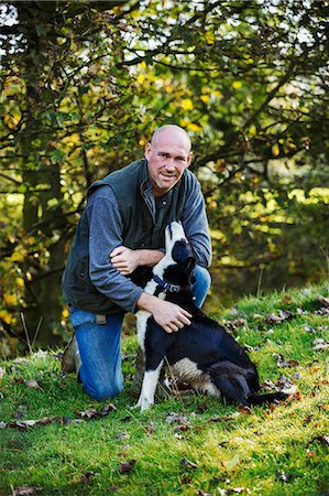 simsearch:400-05724021,k - Sheep farmer kneeling on a meadow patting his black and white sheepdog. Stock Photo - Premium Royalty-Free, Code: 6118-08928270