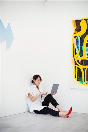 simsearch:693-05552760,k - Woman with short black hair wearing white shirt, black trousers and red high heel shoes sitting on floor i art gallery, holding laptop. Stock Photo - Premium Royalty-Free, Code: 6118-09079475