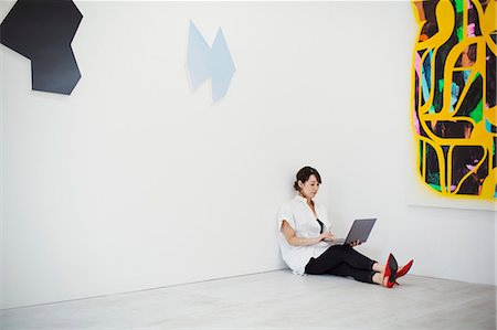 simsearch:614-02985267,k - Woman with short black hair wearing white shirt, black trousers and red high heel shoes sitting on floor i art gallery, holding laptop. Stock Photo - Premium Royalty-Free, Code: 6118-09079476