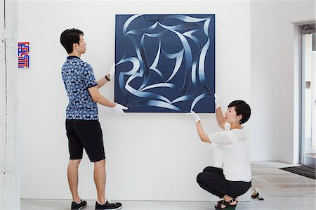 simsearch:693-05552760,k - Man in blue shirt and woman wearing white shirt hanging modern painting on white wall in art gallery. Stock Photo - Premium Royalty-Free, Code: 6118-09079480