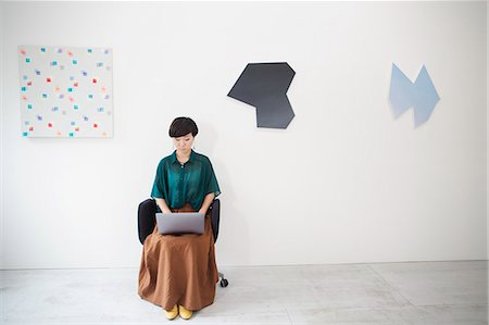 simsearch:614-02985267,k - Woman with short black hair wearing green shirt sitting in art gallery, typing on laptop computer. Stock Photo - Premium Royalty-Free, Code: 6118-09079484
