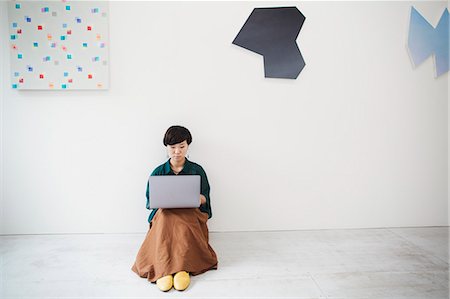 simsearch:614-02985267,k - Woman with short black hair wearing green shirt sitting on floor in art gallery, balancing laptop on her knees. Stock Photo - Premium Royalty-Free, Code: 6118-09079485