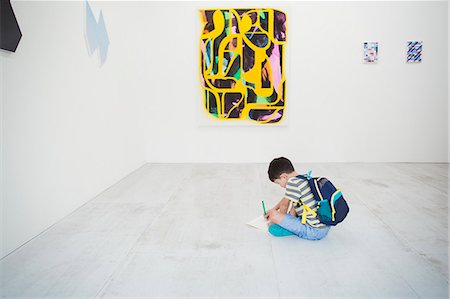 simsearch:693-05552760,k - Boy with short black hair wearing backpack sitting on floor in art gallery with pen and paper, looking at modern painting. Stock Photo - Premium Royalty-Free, Code: 6118-09079488