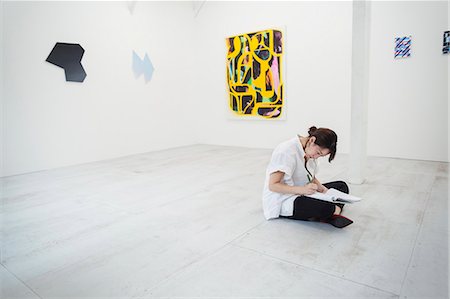 simsearch:693-05552760,k - Woman with black hair wearing white shirt sitting on floor in art gallery with pen and paper. Stock Photo - Premium Royalty-Free, Code: 6118-09079495