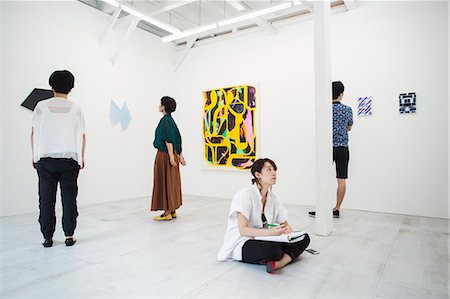 simsearch:693-05552760,k - Woman with black hair sitting on floor in art gallery with pen and paper, looking at modern painting, three people standing in front of artworks. Stock Photo - Premium Royalty-Free, Code: 6118-09079496