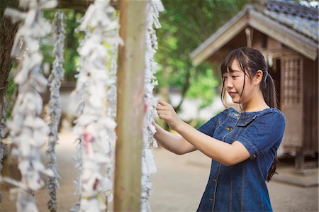 Young woman wearing blue dress tying omikuji fortune telling paper at Shinto Sakurai Shrine, Fukuoka, Japan. Stock Photo - Premium Royalty-Free, Code: 6118-09079562