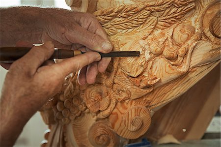 simsearch:6118-08521776,k - Close up of a craftsman at work, using a fine chisel to shape and chisel out the detail in decorations on a wooden figurehead in a workshop. Stock Photo - Premium Royalty-Free, Code: 6118-09018397