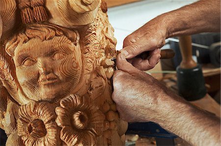 simsearch:6118-08521776,k - Close up of an artisan craftsman, a wood carver working on a wooden figurehead with a human face and floral shapes in a workshop, holding a small chisel. Stock Photo - Premium Royalty-Free, Code: 6118-09018399