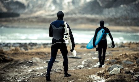 simsearch:6118-09039107,k - Two surfers wearing wetsuits and carrying surfboards walking towards the ocean with mountains behind. Stock Photo - Premium Royalty-Free, Code: 6118-09039180