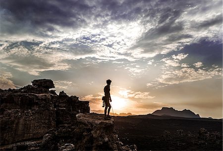 silhouette mountain peak - Mountaineer standing on top of a rock formation in a mountainous landscape. Stock Photo - Premium Royalty-Free, Code: 6118-09039110