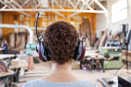 Close up view from behind of a woman factory worker wearing hearing protection in a woodworking factory. Stock Photo - Premium Royalty-Free, Code: 6118-09140141