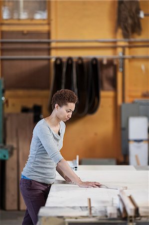 Black woman factory worker measuring wood at a work station in a woodworking factory. Stock Photo - Premium Royalty-Free, Code: 6118-09140153