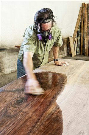 Caucasian man factory worker applying finish to a recycled wood table top in a woodworking factory Stock Photo - Premium Royalty-Free, Code: 6118-09140157