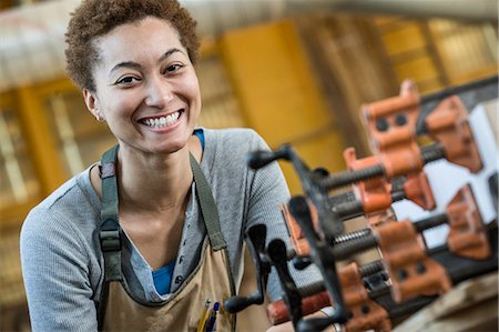 View of a smiling black woman factory worker at her work station in a woodworking factory. Stock Photo - Premium Royalty-Free, Code: 6118-09140163