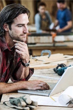 Caucasian man factory worker working on a lap top computer at a work station in a woodworking factory. Stock Photo - Premium Royalty-Free, Code: 6118-09140161