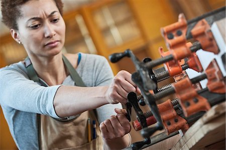Black woman factory worker adjusting clamps while glueing a large wooden part in a woodworking factory. Stock Photo - Premium Royalty-Free, Code: 6118-09140162