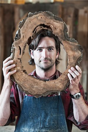 Caucasian man factory worker holding a cut piece from a section of a reclaimed recycled tree in a woodworking factory. Stock Photo - Premium Royalty-Free, Code: 6118-09140171
