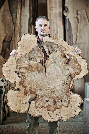 Caucasian man factory worker holding a sawn cross section of a  tree trunk in a woodworking factory using recycled timber. Stock Photo - Premium Royalty-Free, Code: 6118-09140174