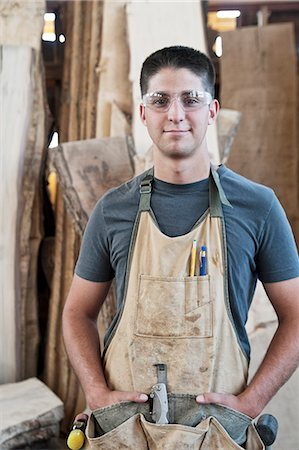 View of a young Caucasian man factory worker wearing an apron in a woodworking factory. Stock Photo - Premium Royalty-Free, Code: 6118-09140119
