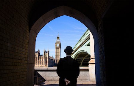 Rear view of man wearing black coat and Bowler hat standing near Westminster Bridge by the River Thames, Big Ben and Houses of Parliament in the distance, London, England. Stock Photo - Premium Royalty-Free, Code: 6118-09144911