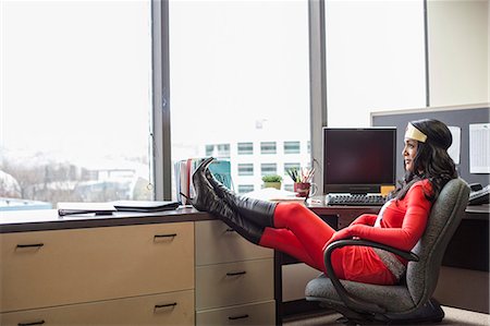 A black office superhero business woman sits in her office and ponders her next business move. Stock Photo - Premium Royalty-Free, Code: 6118-09147978
