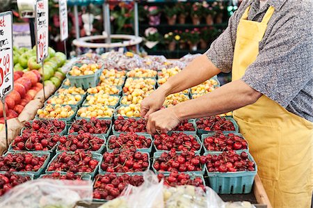 simsearch:614-06169178,k - Man wearing apron standing at stall with punnets of fresh cherries at a fruit and vegetable market. Stock Photo - Premium Royalty-Free, Code: 6118-09148111