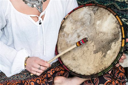 percussion instrument - High angle view of woman wearing trousers with floral pattern sitting on shag carpet, holding shaman drum. Stock Photo - Premium Royalty-Free, Code: 6118-09165847
