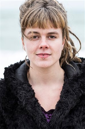 simsearch:400-04435419,k - Portrait of young woman with brown hair and dreadlocks and a lip piercing wearing black furry jacket, looking at camera. Stock Photo - Premium Royalty-Free, Code: 6118-09165845