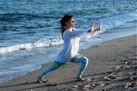 simsearch:6118-07731916,k - Young woman with brown hair wearing white blouse standing on a beach by the ocean, doing Tai Chi. Photographie de stock - Premium Libres de Droits, Code: 6118-09165856