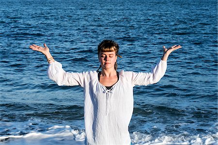 simsearch:6118-07731916,k - Young woman with brown hair wearing white blouse standing on a beach by the ocean, doing Tai Chi. Photographie de stock - Premium Libres de Droits, Code: 6118-09165859