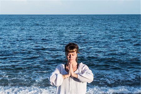 simsearch:6118-07731916,k - Young woman with brown hair wearing white blouse standing on a beach by the ocean, doing Tai Chi. Photographie de stock - Premium Libres de Droits, Code: 6118-09165860