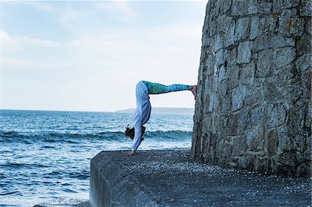 simsearch:6118-07731916,k - Young woman doing handstand by the ocean, with her legs against a wall. Photographie de stock - Premium Libres de Droits, Code: 6118-09165861