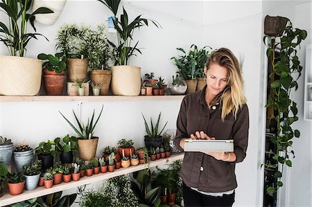 simsearch:6118-08202525,k - Female owner of plant shop standing next to a selection of plants on wooden shelves, holding digital tablet. Stock Photo - Premium Royalty-Free, Code: 6118-09165895