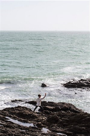 simsearch:6118-07731916,k - Young woman with brown hair and dreadlocks wearing white blouse standing on rocky shore by ocean, doing Tai Chi. Photographie de stock - Premium Libres de Droits, Code: 6118-09165825