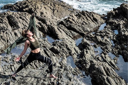 simsearch:6118-07731916,k - Young woman with brown hair and dreadlocks wearing sportswear standing on rocky shore by ocean, doing Tai Chi. Photographie de stock - Premium Libres de Droits, Code: 6118-09165833