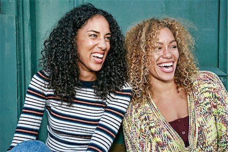 Portrait of two young smiling women with long curly black and blond hair, smiling and laughing. Stock Photo - Premium Royalty-Free, Code: 6118-09165926